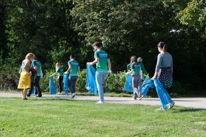 Mitarbeitende von Fujifilm laufen über eine Wiese und sammeln Müll ein.