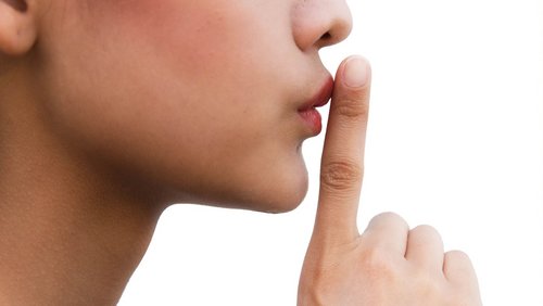 Frau hält einen Zeigefinger vor den Mund