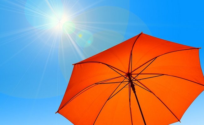 Man sieht einen wolkenfreien Himmel. Die Sonne scheint stark auf einen zum Sonnenschirm umfunktionierten Regenschirm.