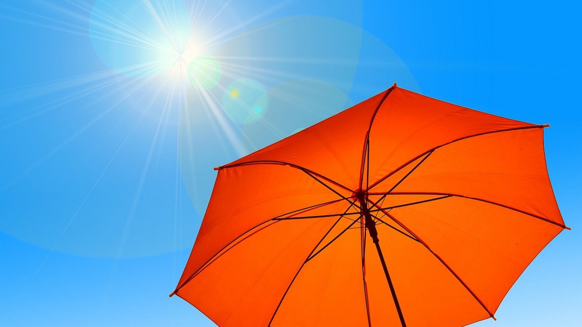 Man sieht einen wolkenfreien Himmel. Die Sonne scheint stark auf einen zum Sonnenschirm umfunktionierten Regenschirm.