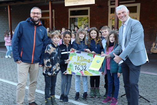 Zwei Männer und mehrere Kinder mit Plakat und Urkunde