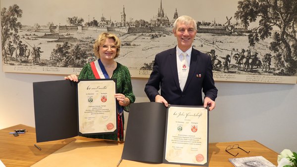 Bürgermeister Klaus Pesch und Bürgermeisterin Marie-Sophie Lesne der Partnerstadt Le Quesnoy halten Urkunden zur Bekräftigung der Städtepartnerschaft in die Kamera