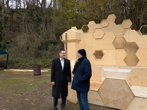 Zwei Männer vor einem Holzbau mit Wabenmuster