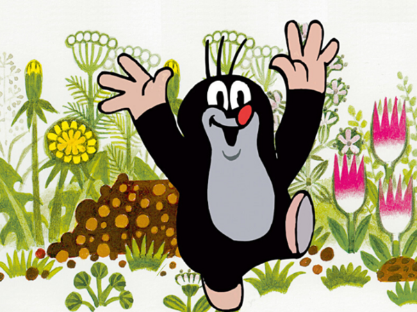 Zeichentrickfigur "Der kleine Maulwurf" steht mit ausgebreiteten Armen inmitten einer Blumenwiese. 