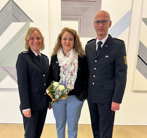 Frau mit Blumenstrauß in der Mitte, links und rechts Frau bzw. Mann mit Uniform