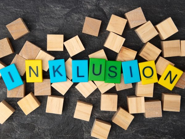 Mehrere Holzwürfel liegen auf einem Tisch, farbige Würfel bilden das Wort Inklusion 