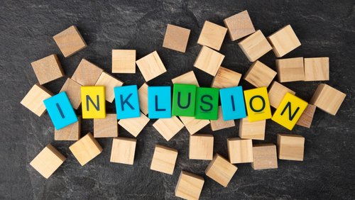 Mehrere Holzwürfel liegen auf einem Tisch, farbige Würfel bilden das Wort Inklusion 
