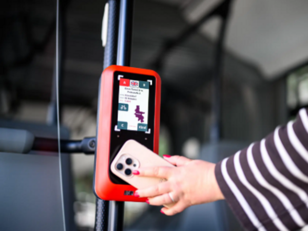 Eine Hand hält ein Smartphone vor ein rotes Lesegerät in einem Bus.