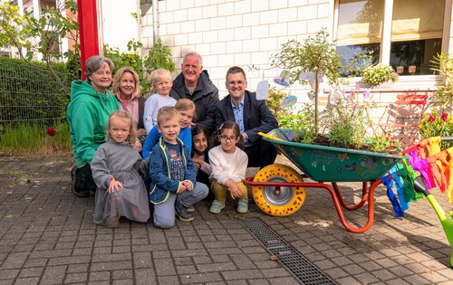 Mehrere Kinder und Erwachsene in der Hocke, daneben steht eine bepflanzte Schubkarre