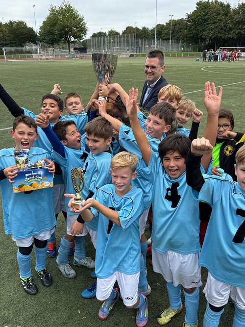 Jungs in hellblauen Trikots jubeln und halten einen großen Pokal 