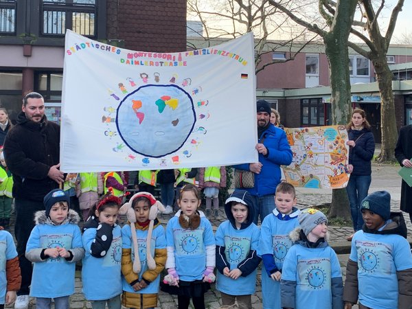 Kindergruppe, dahinter mehrere Personen mit einem Banner 