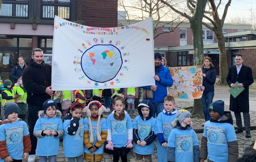 Kindergruppe, dahinter mehrere Personen mit einem Banner 