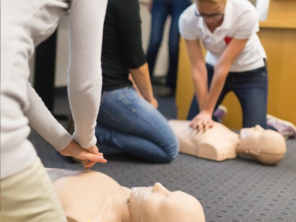 Zwei Personen üben auf dem Boden Herzmassage an einer Übungspuppe