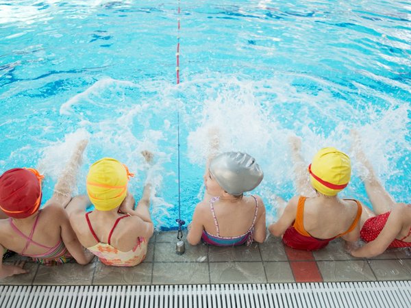 Kinder sitzen am Beckenrand und plantschen mit ihren Füßen im Wasser