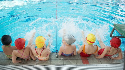 Kinder sitzen am Beckenrand und plantschen mit ihren Füßen im Wasser