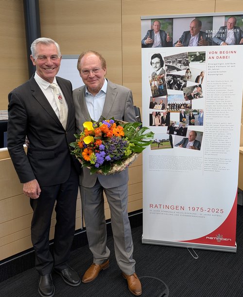 Zwei Männer, einer mit Blumenstrauß, neben einem Rollup 