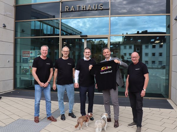 Fünf Männer stehen vor dem Eingang des Rathauses, einer hält ein schwarzes T-Shirt mit dem Aufdruck „Westbahnlauf“ hoch.