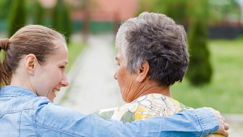 Junge Frau legt älterer Frau den Arm um die Schultern 