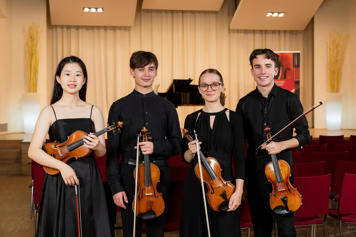 Vier Preisträger stehen nebeneinander und halten ihre Violinen in der Hand. 