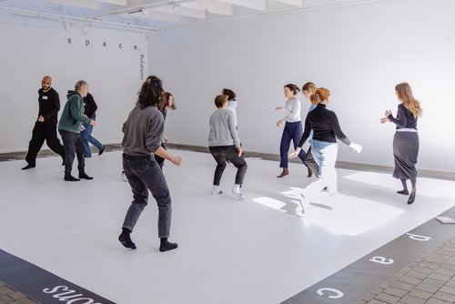 Mehrere Personen bewegen sich tänzerisch durch einen Raum 