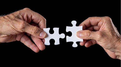 Zwei Hände führen zwei Puzzlestücke zusammen