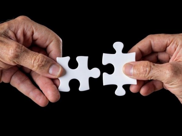 Zwei Hände führen zwei Puzzlestücke zusammen