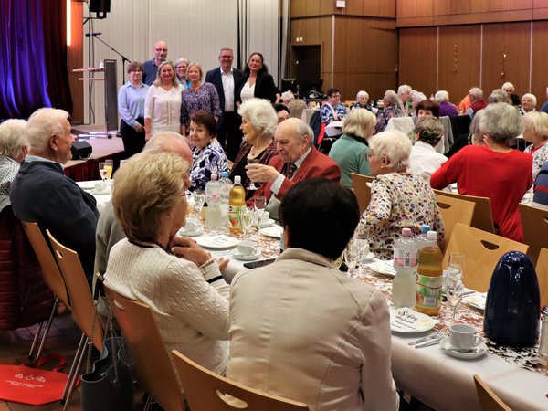 Viele ältere Menschen sitzen an Tischen in einem Saal und feiern zusammen