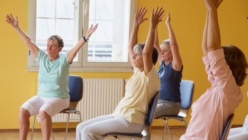 Frauen sitzen auf einem Stuhl und strecken die Arme in die Höhe 
