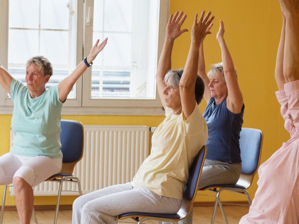 Frauen sitzen auf einem Stuhl und strecken die Arme in die Höhe 