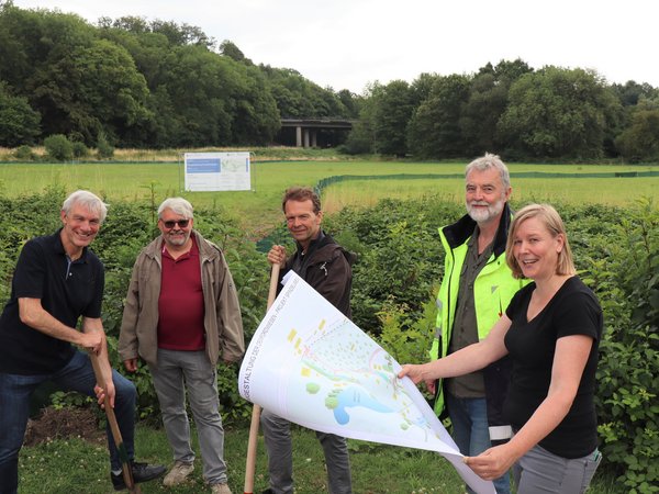 Mehrere Personen mit Spaten oder Plan vor einer grünen Wiese