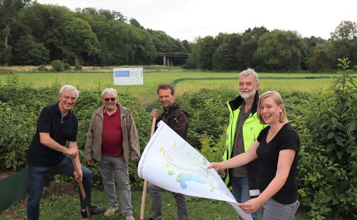 Mehrere Personen mit Spaten oder Plan vor einer grünen Wiese