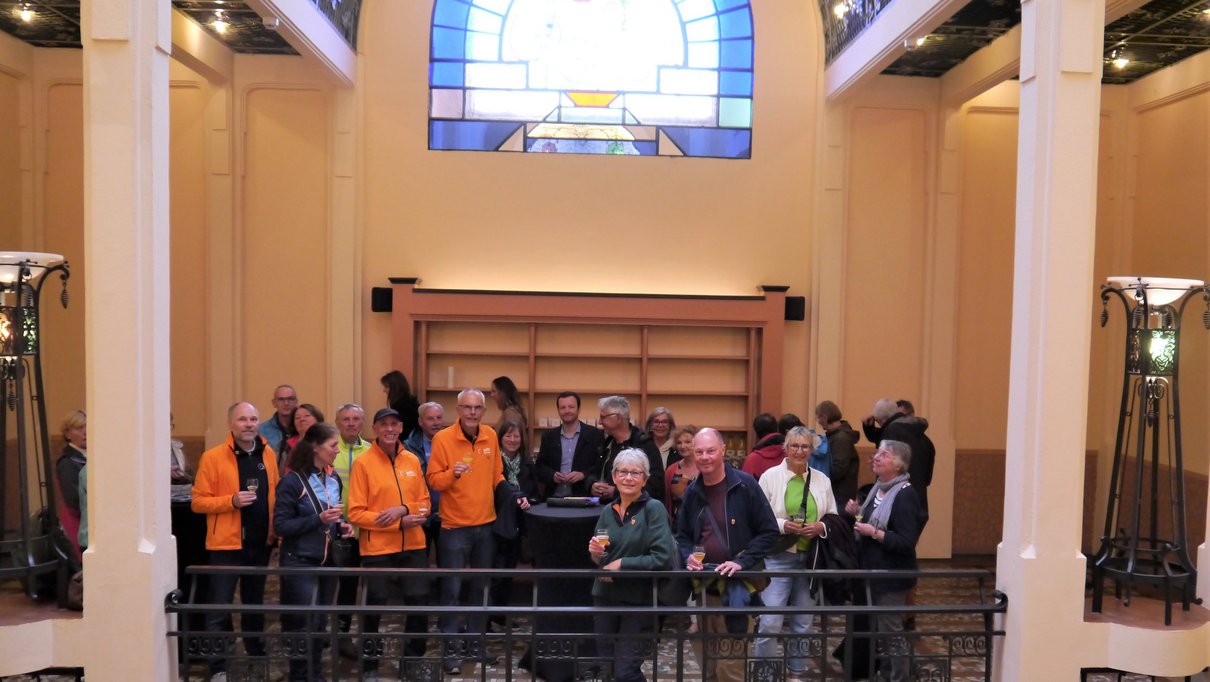 Menschengruppe in Saal unter Jugendstilfenster