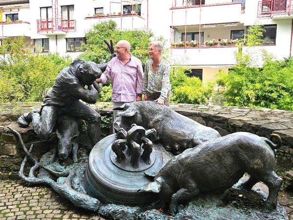 Zwei Personen an einer bronzenen Skulpturengruppe mit einem Schweinehirten und mehreren Schweinen