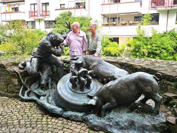 Zwei Personen an einer bronzenen Skulpturengruppe mit einem Schweinehirten und mehreren Schweinen