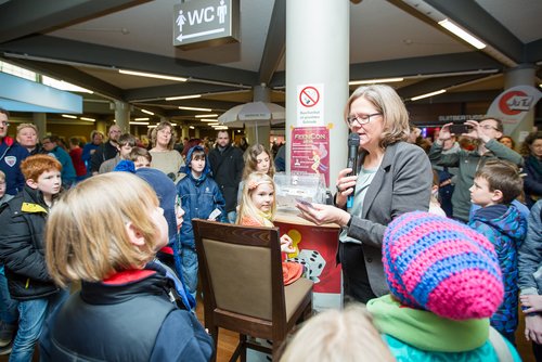 Frau mit Mikrofon an einer Tombola, umringt von Kindern und Erwachsenen 