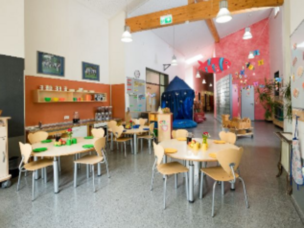 Kita-Raum mit kleinen Tischen, Stühlen und Spielbereich