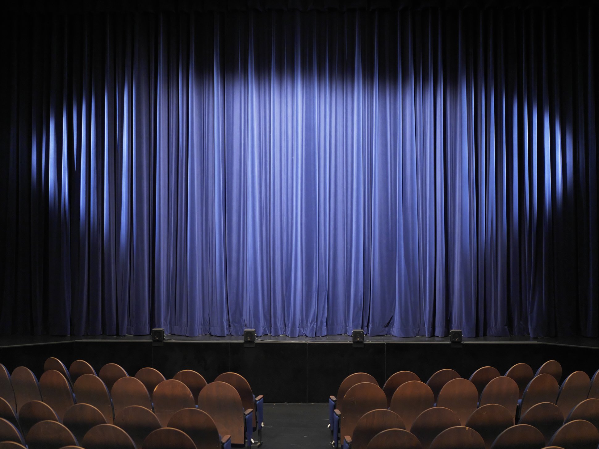 Theatersaal mit roten Sitzen und Blick auf die Bühne mit blauem Vorhang
