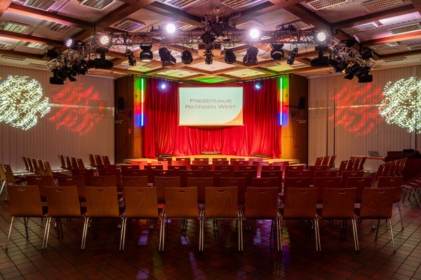 Saal des Freizeithauses, bestuhlt und die Bühne ist farbig beleuchtet. 
