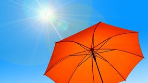 roter Sonnenschirm vor blauen Himmel mit stechender Sonne