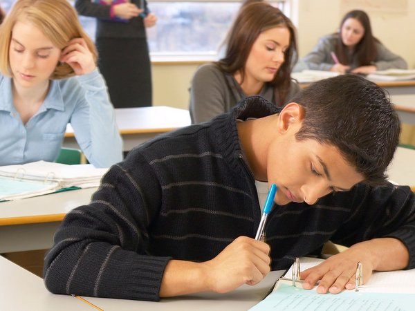 Schüler sitzen mit mit Heften und Stiften an Tischen