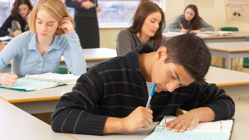 Schüler sitzen mit mit Heften und Stiften an Tischen