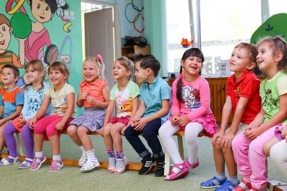 Kinder sitzen in einer Kita nebeneinander auf Stühlen