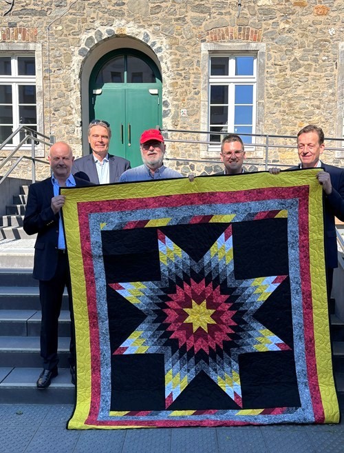 Fünf Männer halten einen indianischen Star Quilt in die Höhe